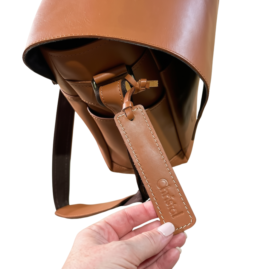 A close-up of the Unico leather weekend bag with a matching leather personalized hangtag held by a hand. 