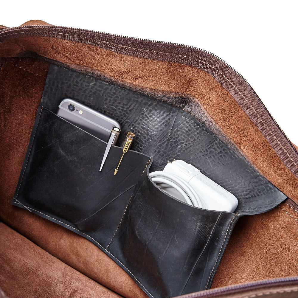 Gabriel leather messenger bag by Miina Goods with an upcycled tire pocket containing a smartphone, pen, and papers.