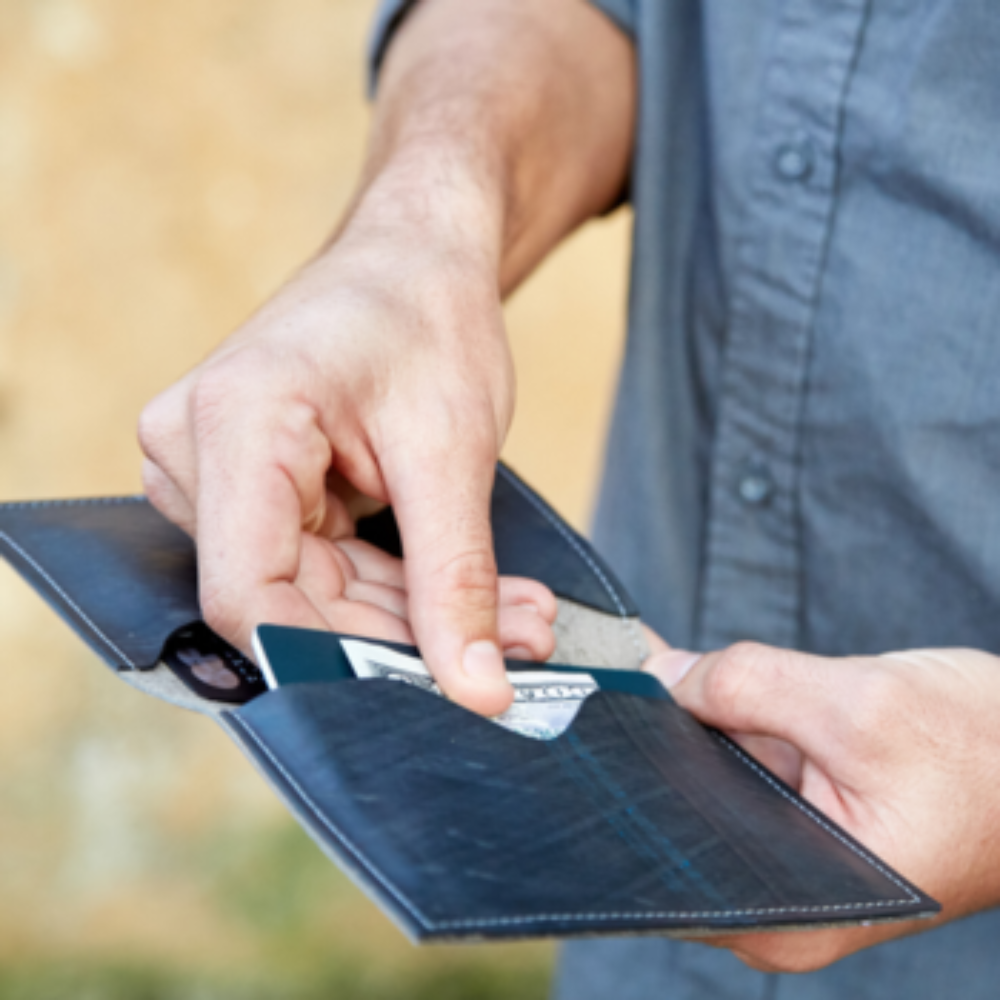 Male model holding a blue Pearson upcycled leather passport holder with a blurred background