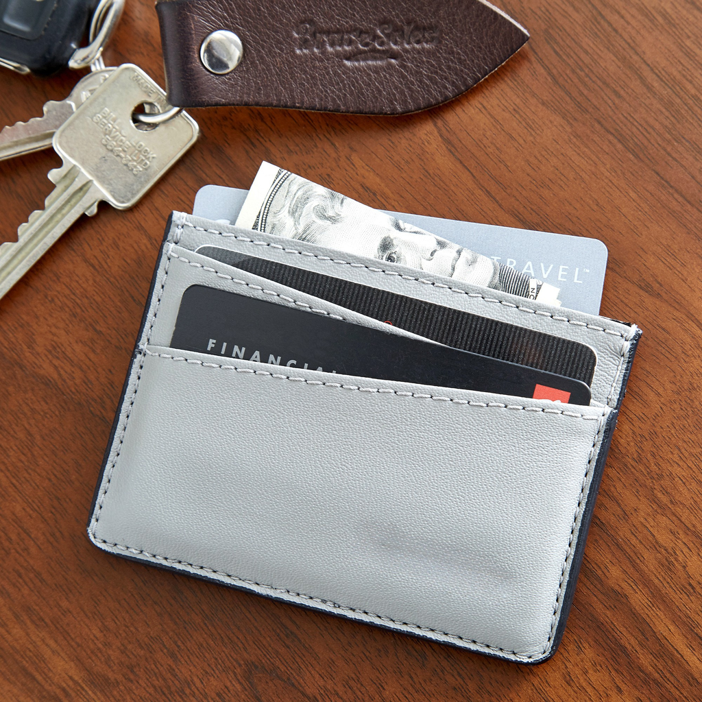 Gray cardholder with cards and money on a wooden surface with keys and a leather pouch.