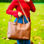 Christal leather tote in caramel front view being held by model wearing a red shirt and blue jeans